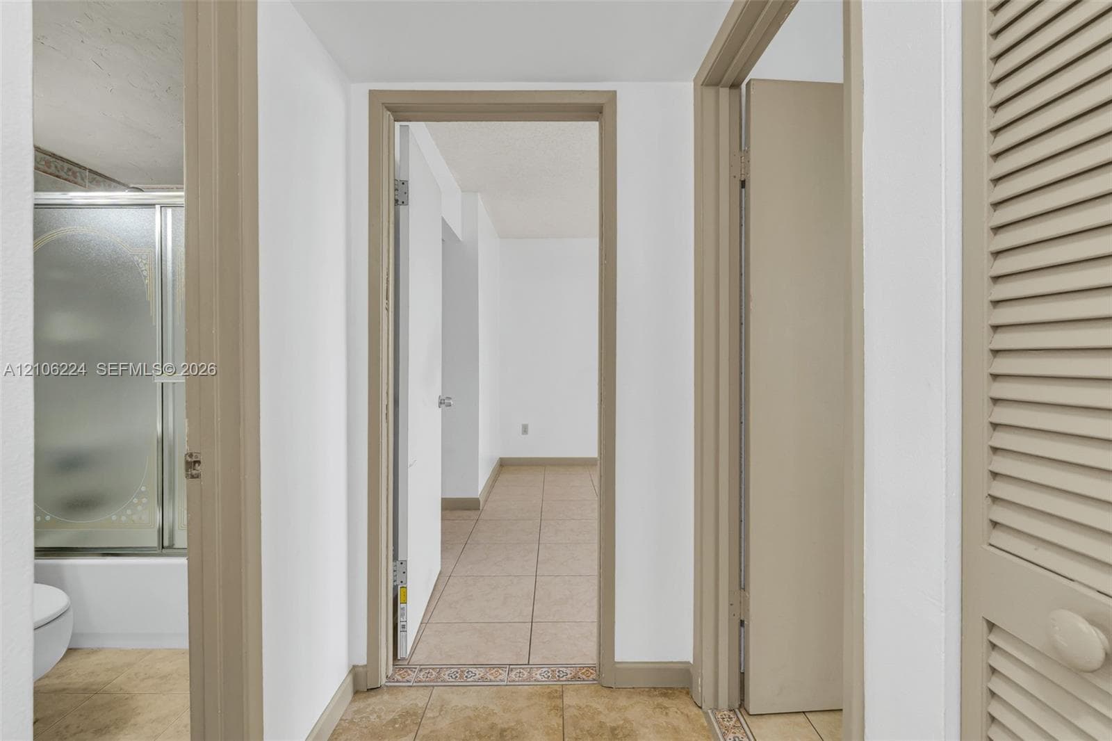 Hallway featuring neutral-tone tile flooring, neutral wall finishes, and a louvered closet door