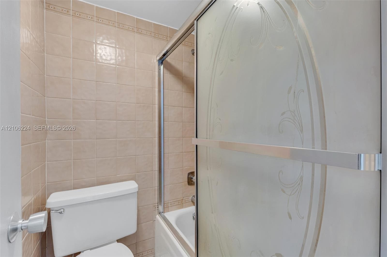 Full-height square wall tile, sliding shower door with decorative etched detailing, and integrated bathtub