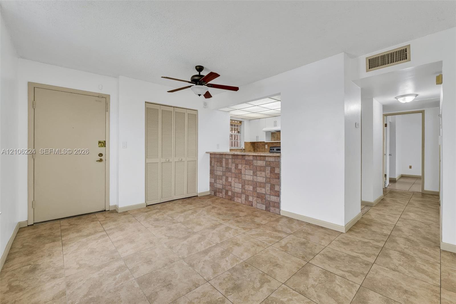 Open floor plan featuring tile flooring, a stone-tiled breakfast bar, built-in louvered-door closet, and ceiling fan