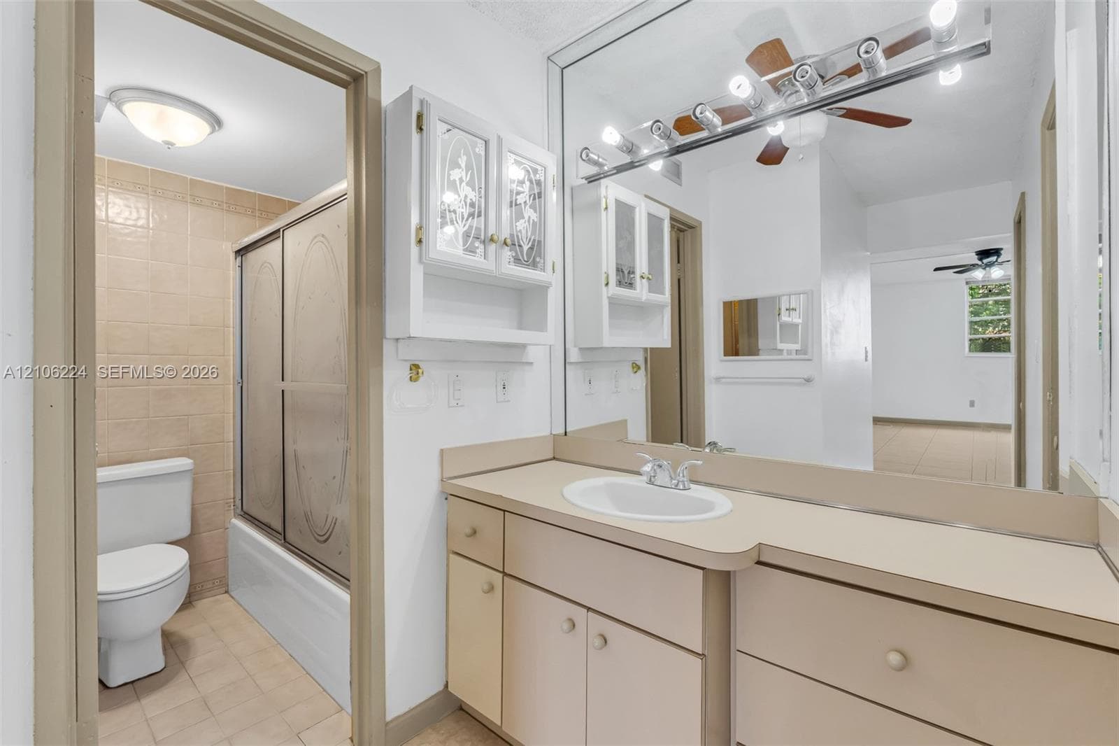 Full-width vanity with integrated basin, expansive wall-to-wall mirror, cabinetry with glass-panel doors, and a tiled shower enclosure