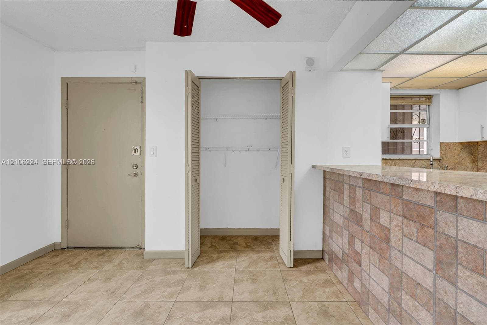Ceramic tile flooring, louvered bi-fold closet doors, a kitchen peninsula with a stone-finish countertop and tiled base, and recessed ceiling lighting