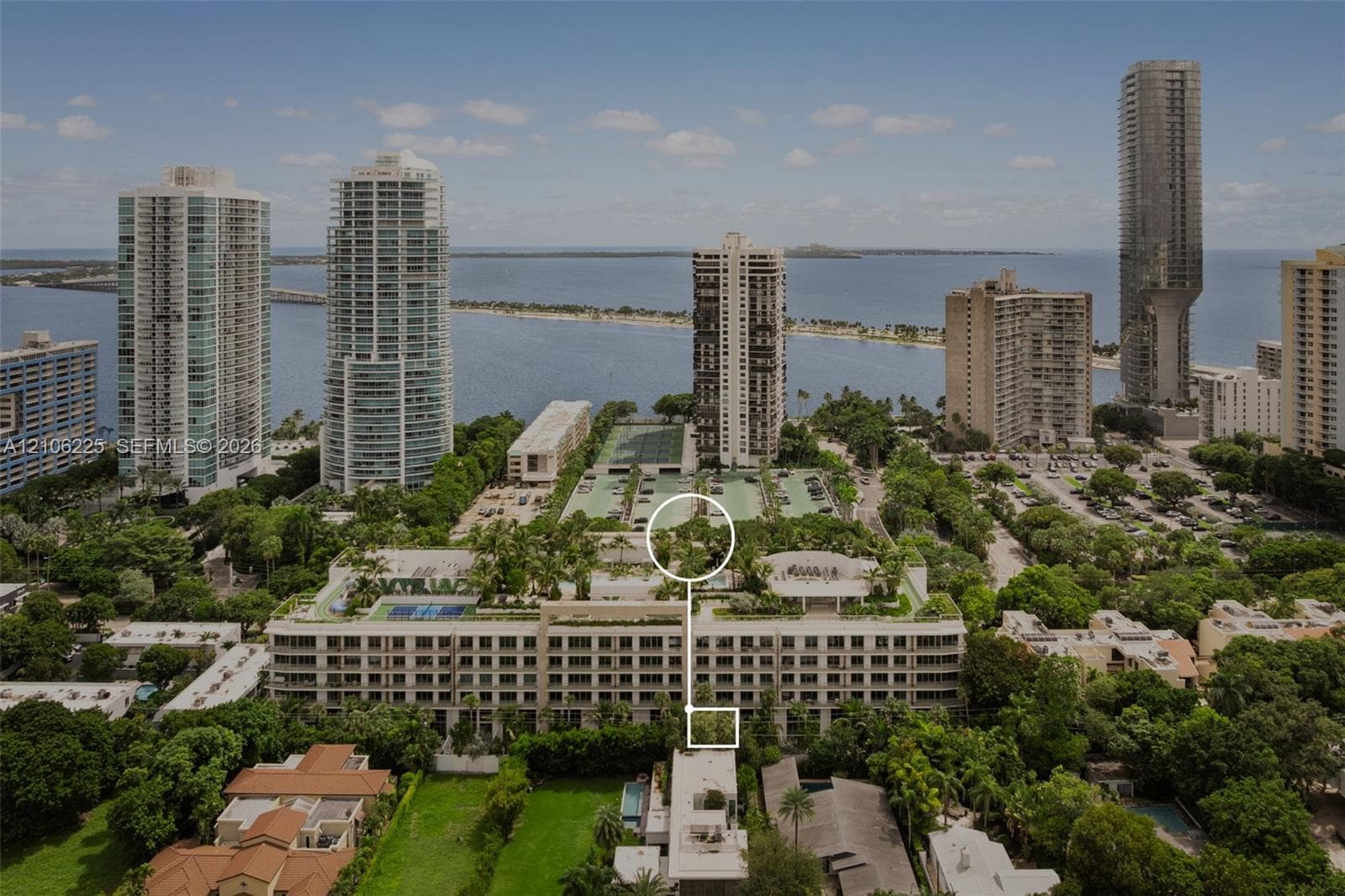 Aerial perspective of a multi-story residential building featuring rooftop recreational facilities, landscaped gardens, multiple tennis courts, and mature perimeter trees