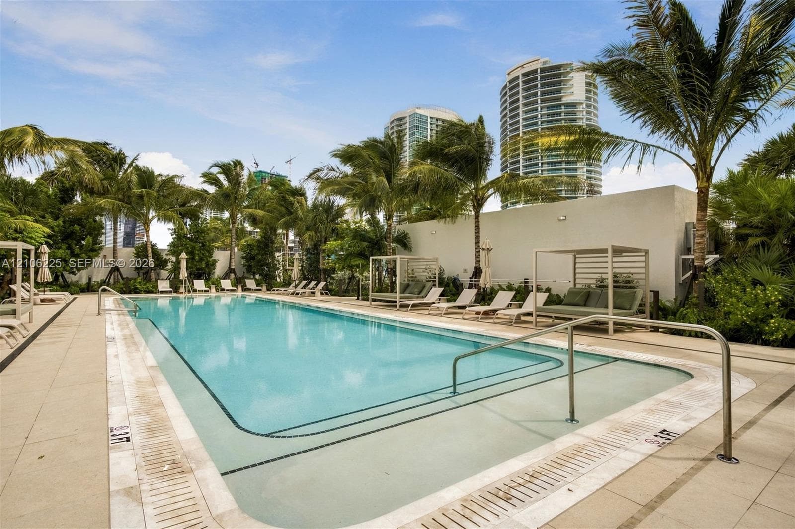 Swimming pool featuring a concrete deck, submerged entry steps, metal handrails, and surrounding palm trees