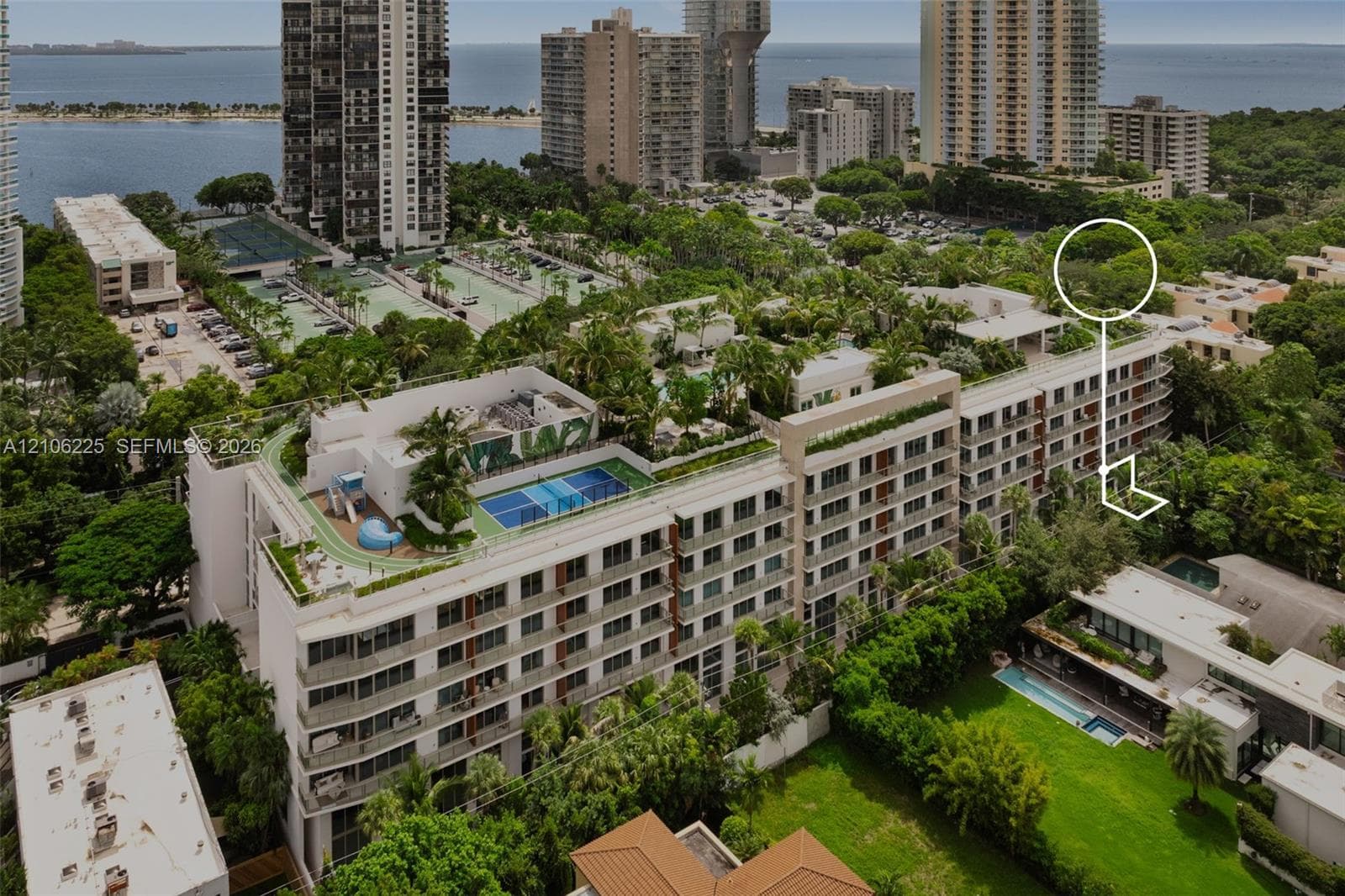 Aerial perspective of a multi-story residential building featuring a landscaped rooftop with a swimming pool, tennis court, and lush garden areas