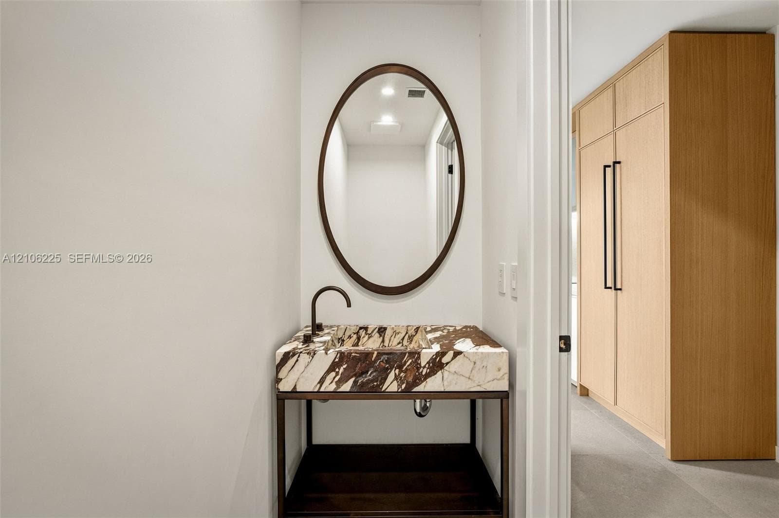 Custom console vanity featuring a stone countertop with integrated basin, oval wall-mounted mirror, matte black faucet, and floor-to-ceiling built-in wood cabinetry