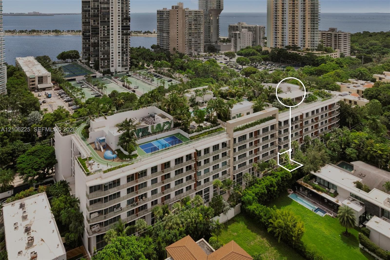 Aerial perspective of a multi-story residential building featuring a rooftop tennis court, landscaped terrace areas, and exterior balconies