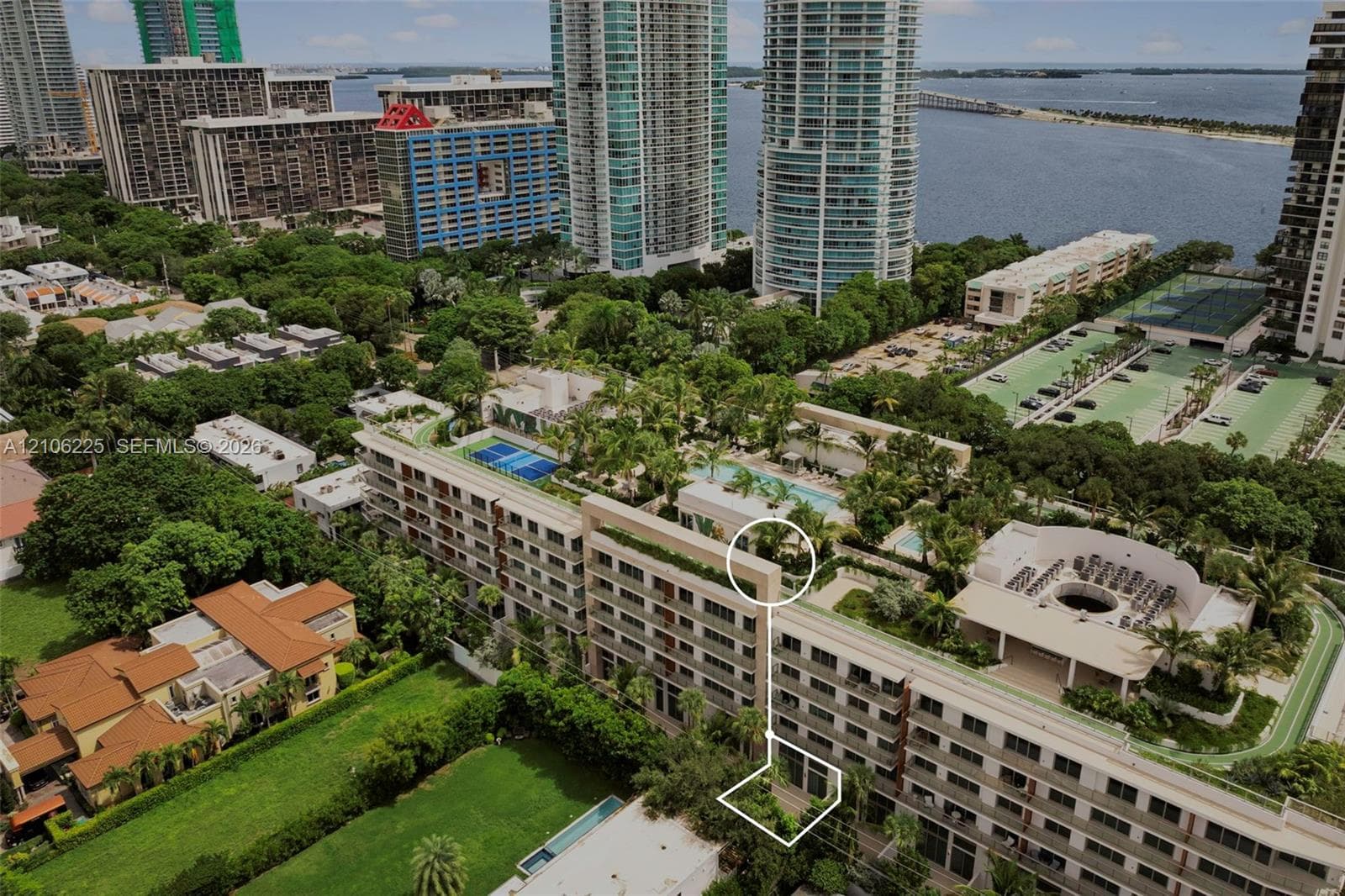 Aerial perspective featuring a multi-story residential building with a landscaped rooftop pool, recreational court, and ground-level private garden area