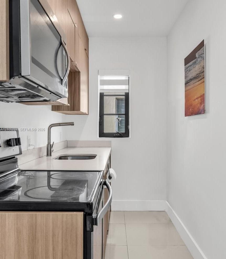 Kitchen featuring flat-panel wood-finish cabinetry, light-toned solid surface countertops, stainless steel appliances, and large-format tile flooring