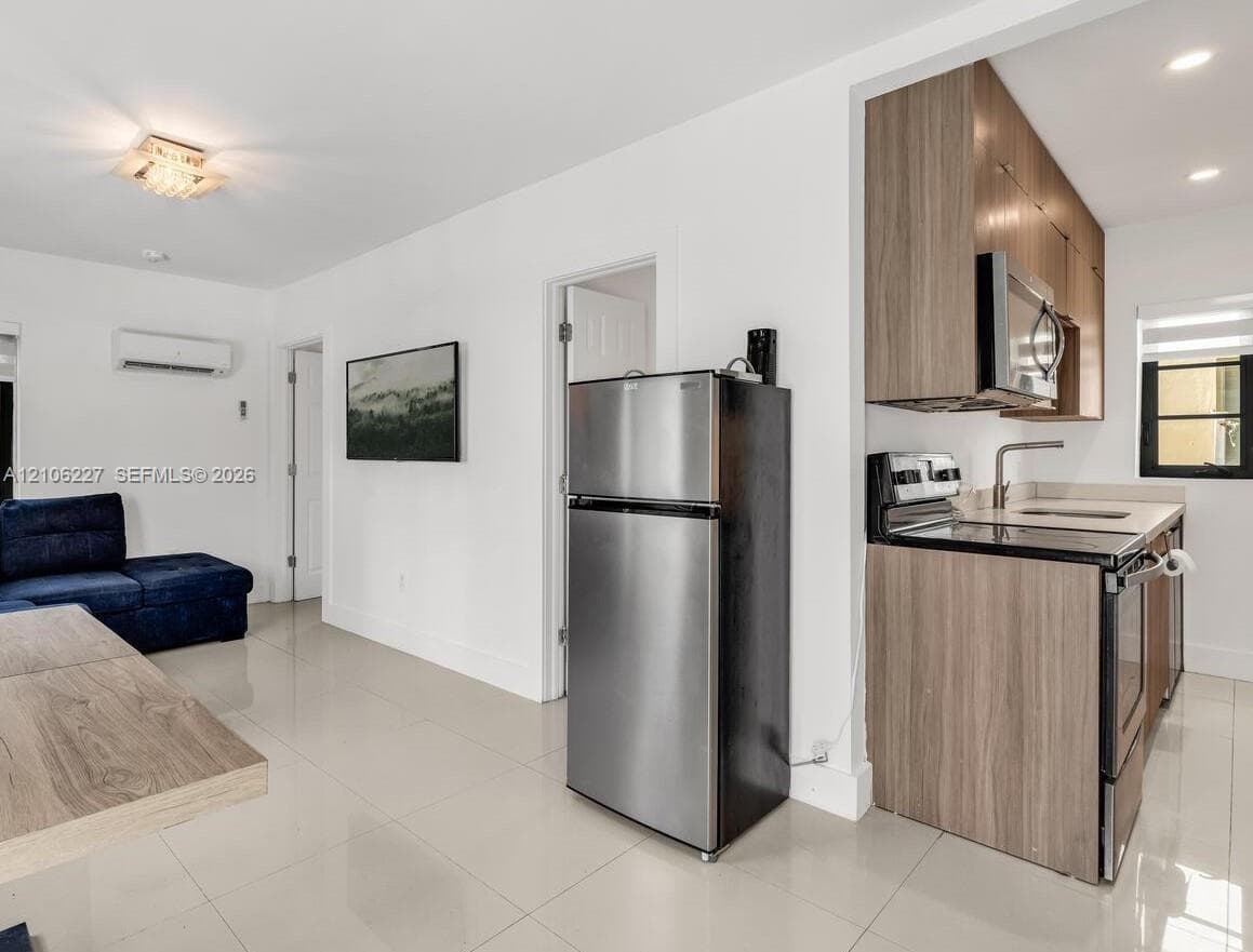 Kitchen featuring wood-finish cabinetry, stainless steel appliances, and solid-surface countertops, paired with tile flooring throughout the area