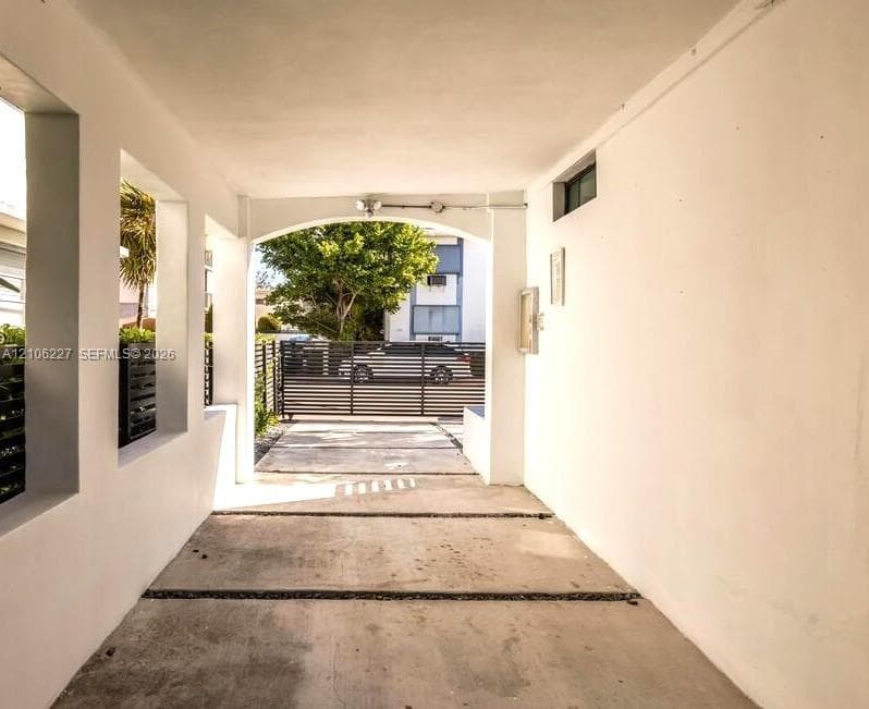 Covered carport featuring an arched entryway, smooth stucco finish, concrete slab flooring, and a metal security gate