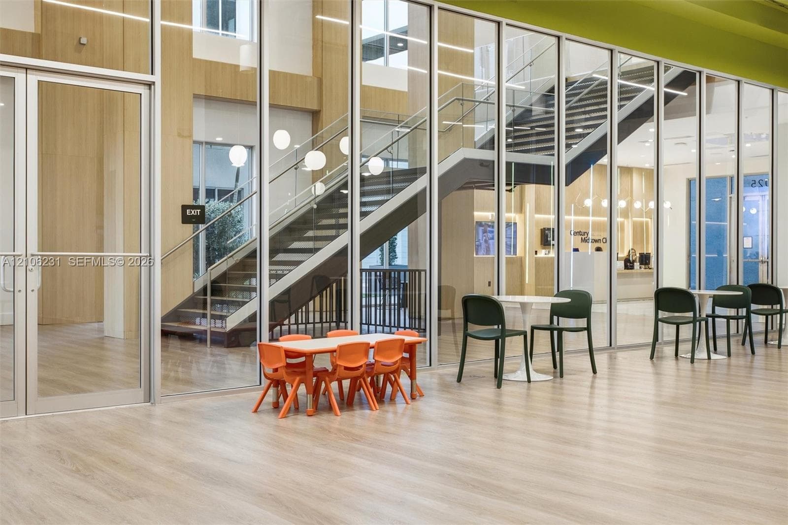 Expansive floor-to-ceiling glass wall partitions, wood-finish flooring, and an open staircase with metal handrails