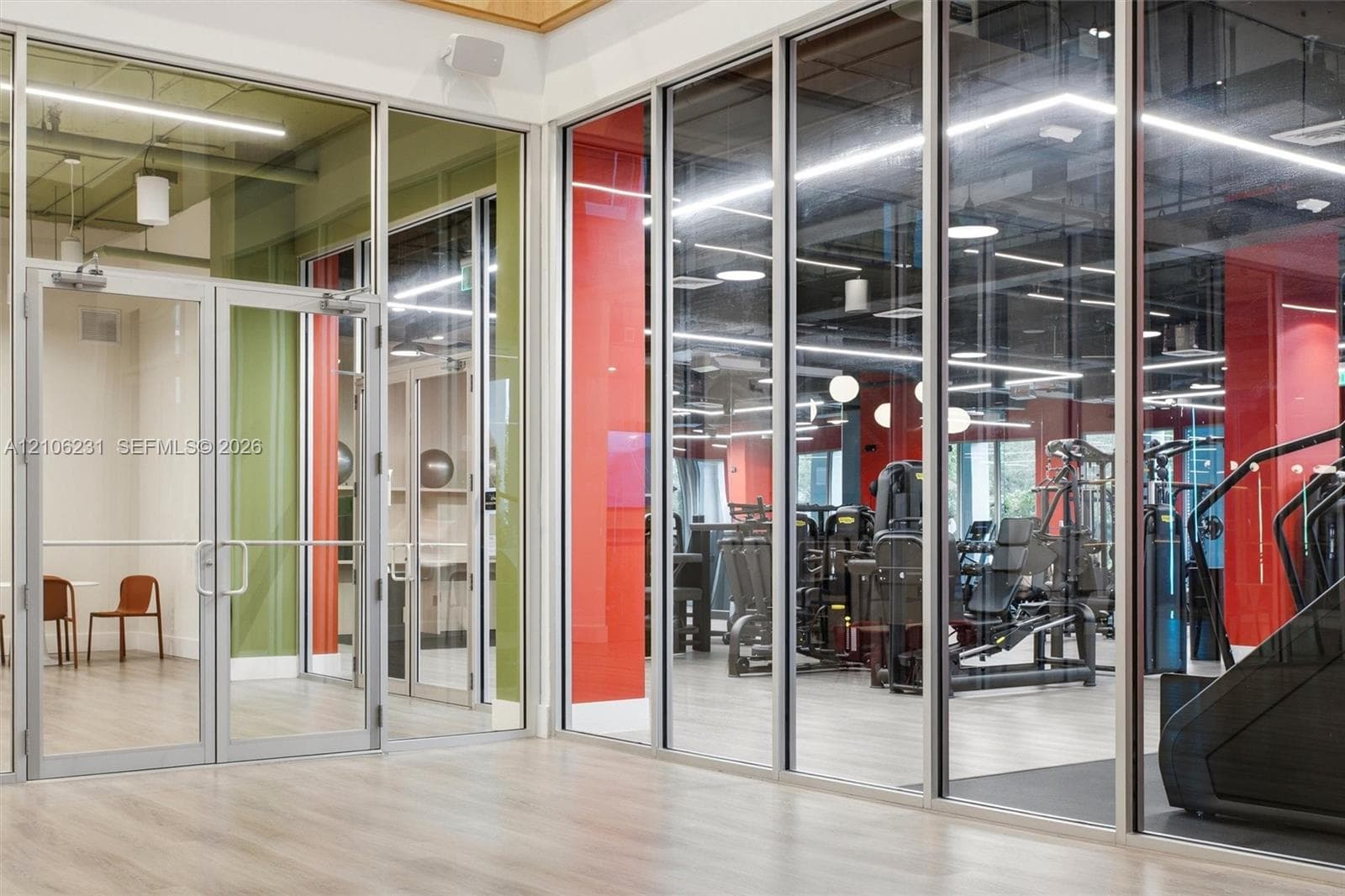 Floor-to-ceiling glass wall partitions with metal framing, wood-finish flooring, exposed ceiling elements, and recessed linear lighting