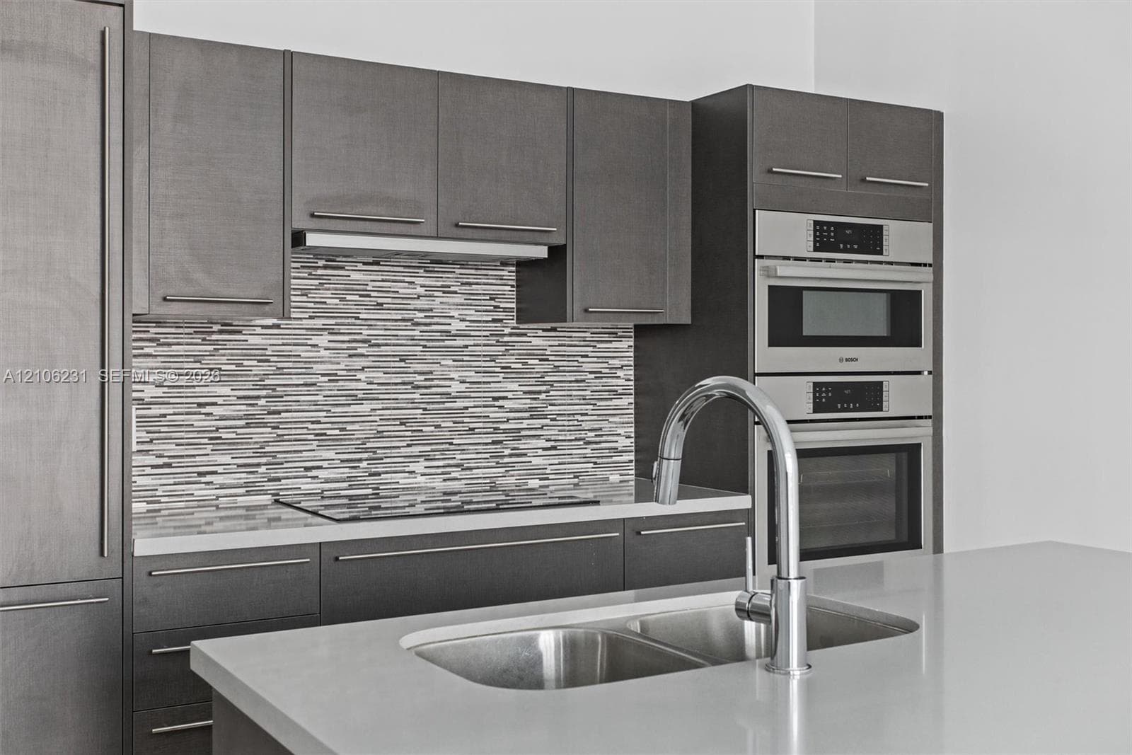 Flat-panel cabinetry, stacked stone tile backsplash, stone countertop, stainless steel double-basin sink with pull-down faucet, and built-in Bosch stainless steel double oven