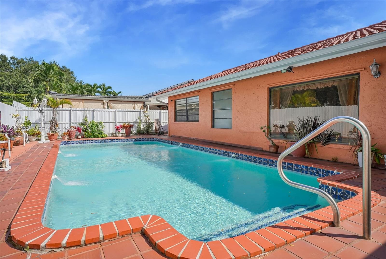 In-ground swimming pool with built-in water features, terracotta-style tiled patio, and privacy fencing