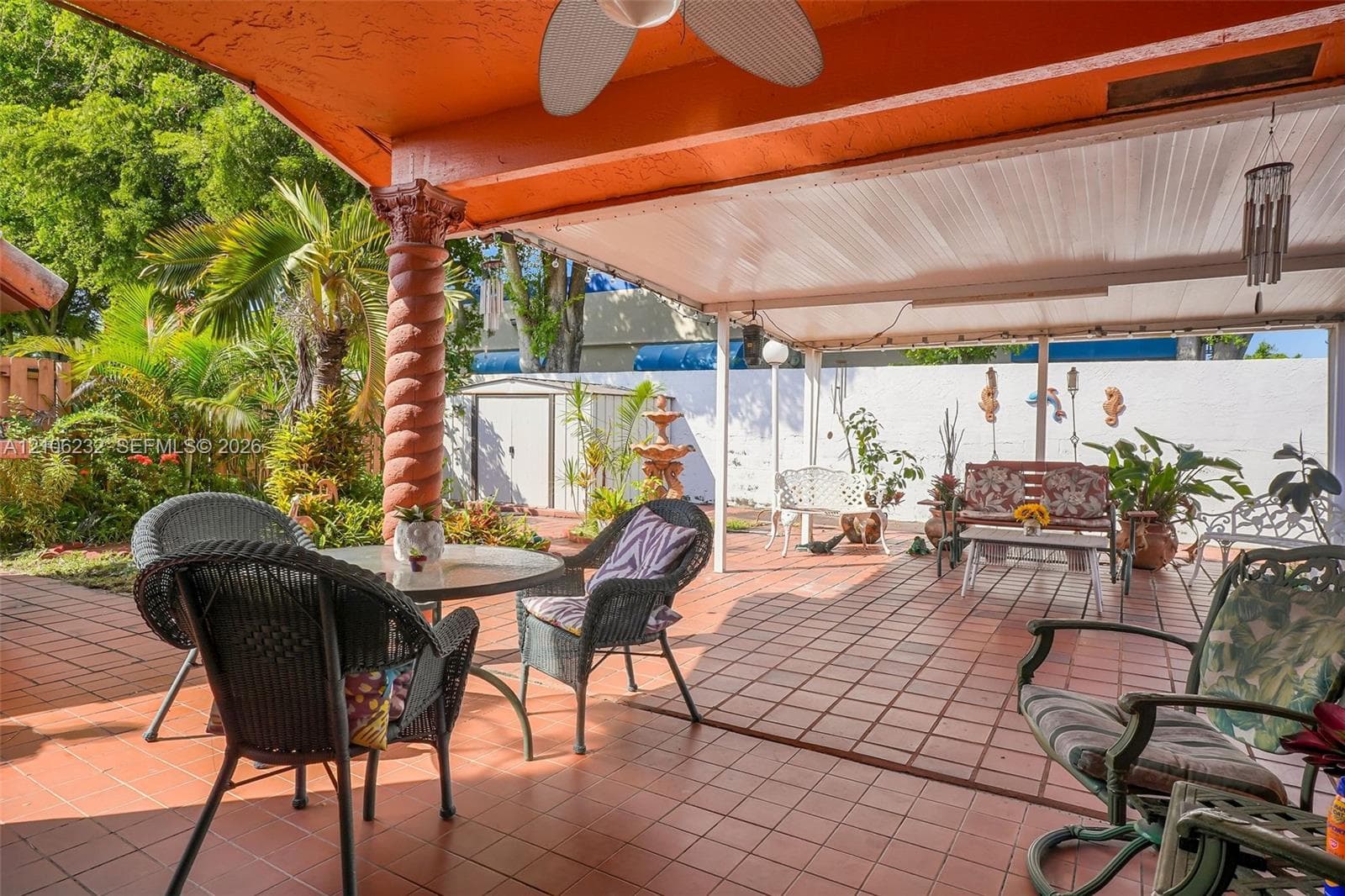 Covered patio featuring terra cotta tile flooring, a decorative spiral column, a ceiling-mounted fan, and an enclosed backyard with a perimeter wall