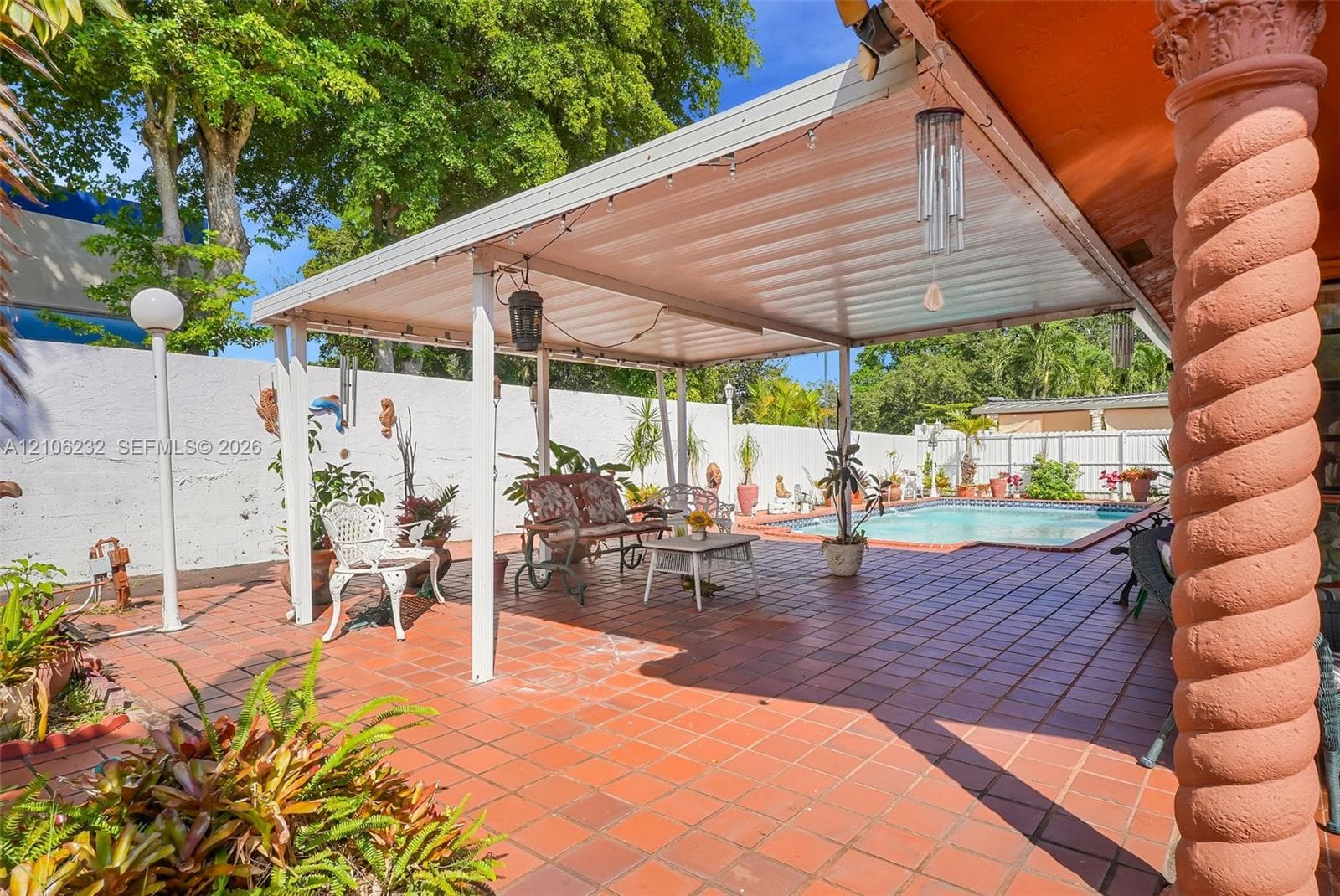 Expansive patio featuring terra cotta tile flooring, a covered metal pergola, a spiraled architectural pillar, and an in-ground swimming pool enclosed by a solid masonry wall