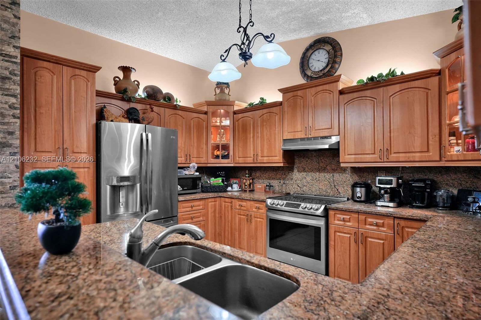 Kitchen featuring wood cabinetry, stone countertops, stainless steel appliances, a dual-basin stainless steel sink, and a decorative chandelier