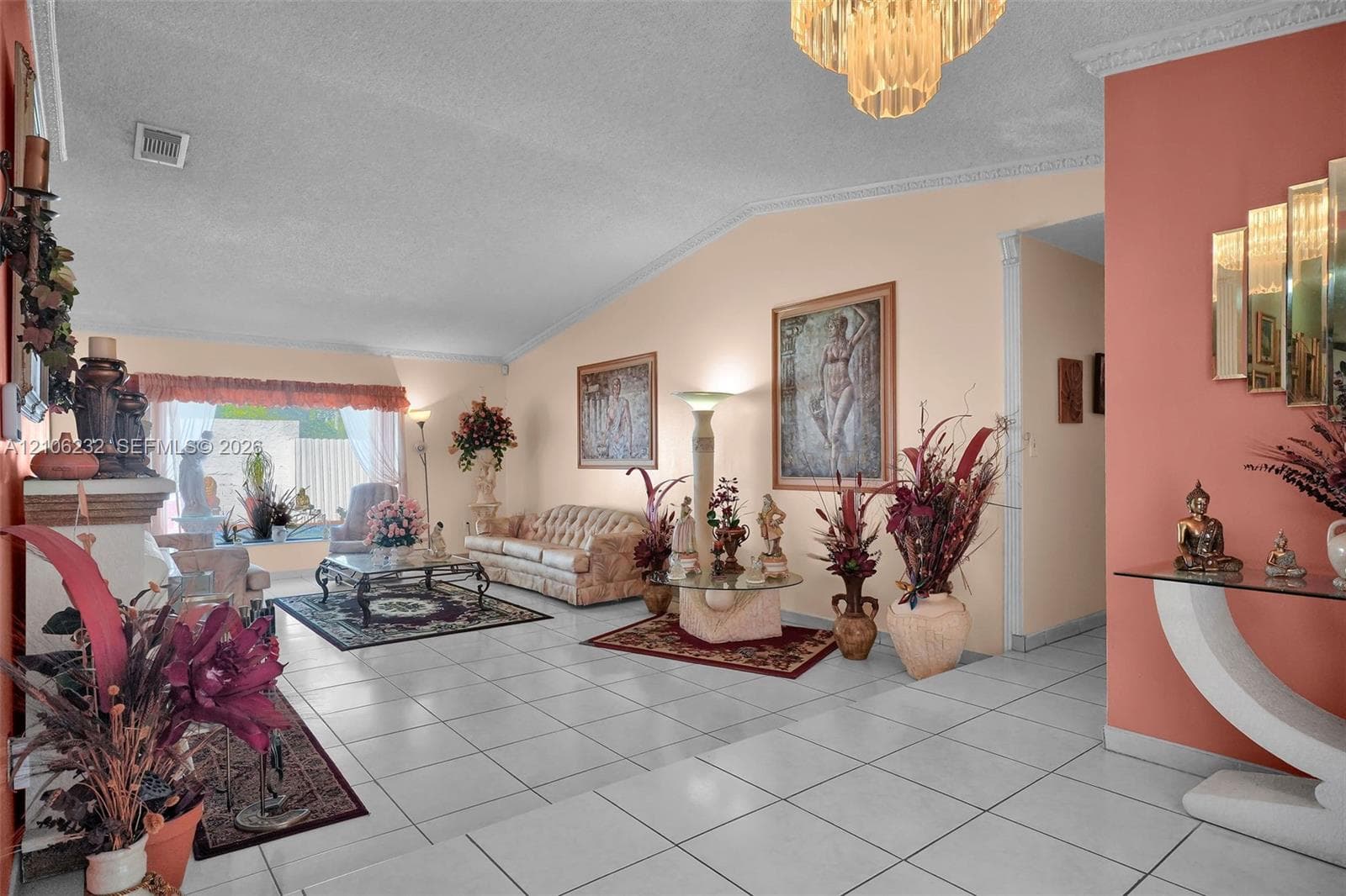 Vaulted ceiling with decorative crown molding and an integrated chandelier, complemented by neutral tile flooring