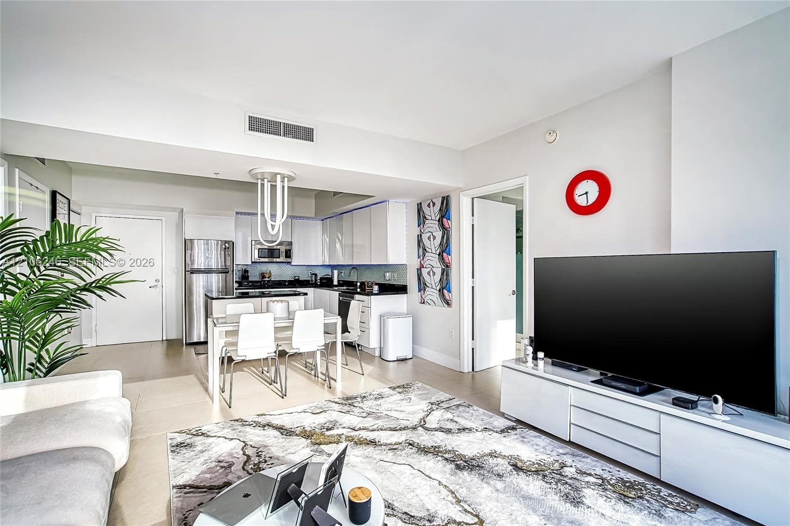 Open-concept kitchen featuring high-gloss white cabinetry, contrasting dark countertops, stainless steel appliances, and a modern sculptural pendant light fixture