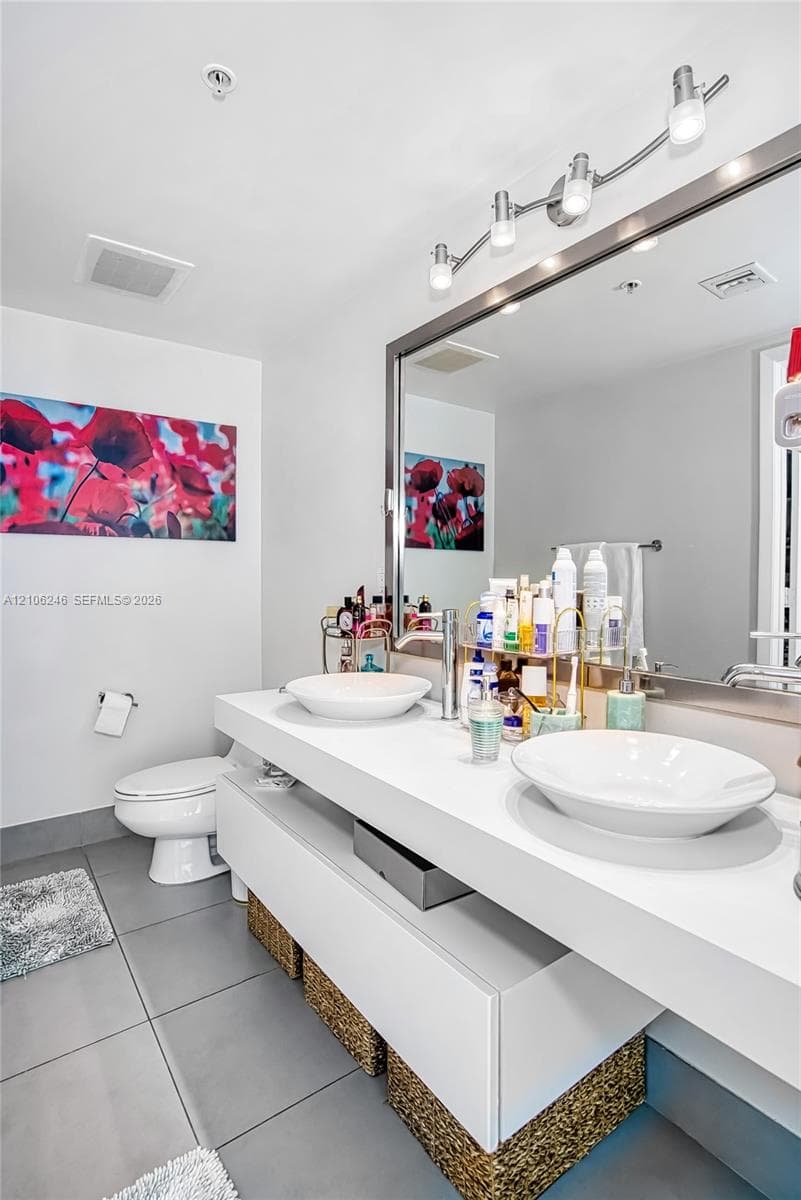 Floating vanity featuring dual white vessel sinks, expansive countertop, large framed wall mirror, and modern multi-bulb overhead lighting fixture