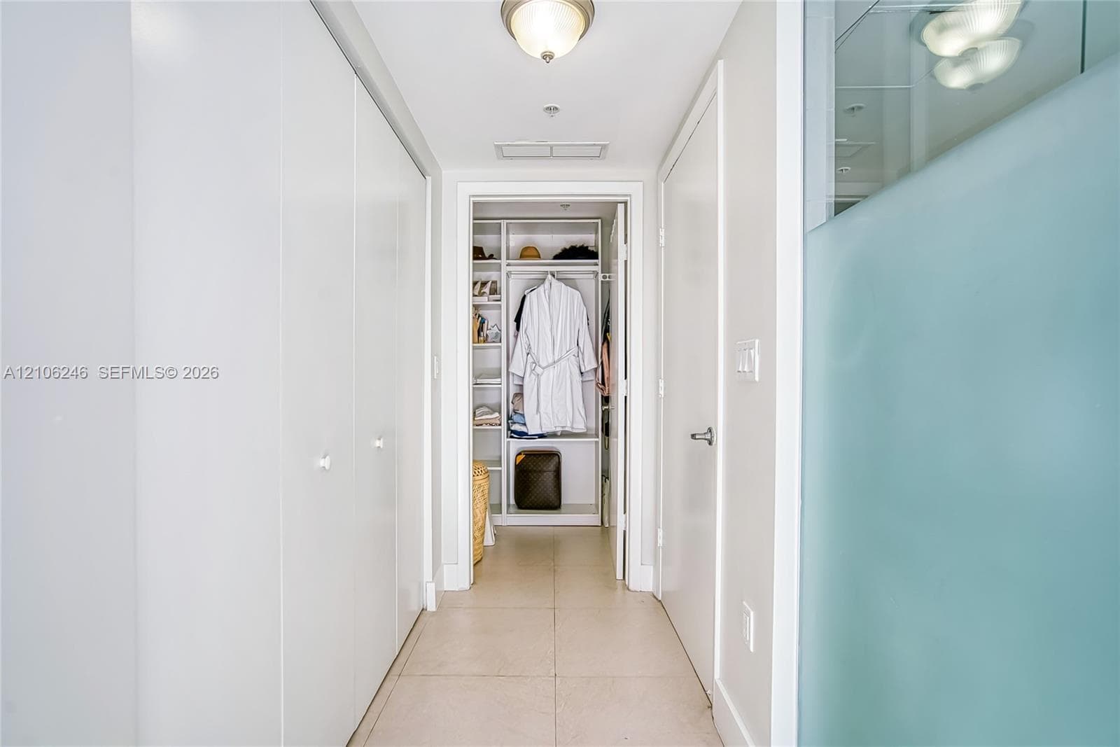 Hallway featuring large-format tile flooring, ceiling-mounted light fixtures, extensive floor-to-ceiling built-in cabinetry, and a walk-in closet with integrated shelving