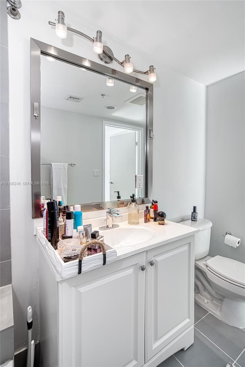 White vanity featuring a smooth countertop with an integrated basin, polished metal hardware, a large framed mirror, and four-light vanity fixture