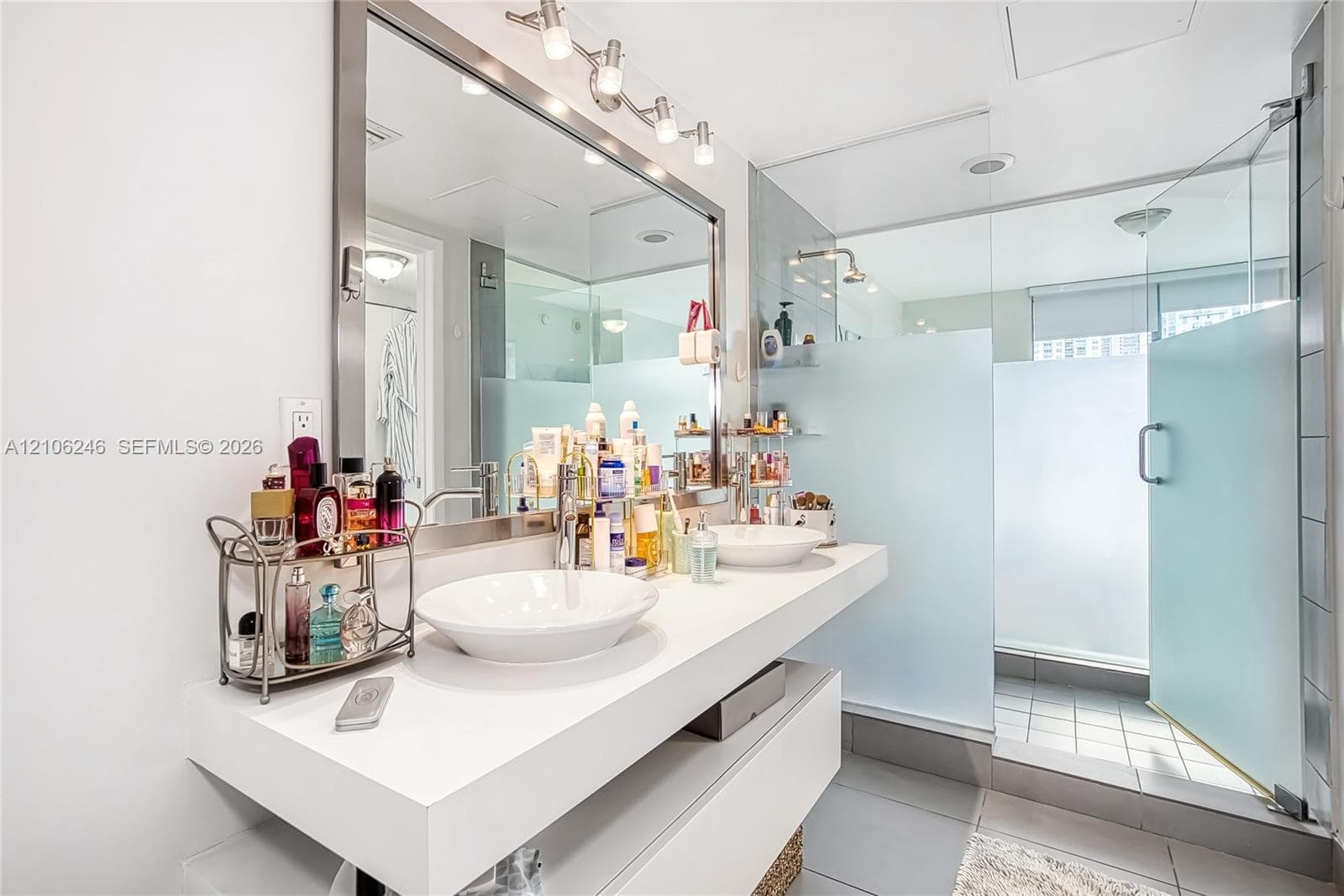 Floating dual-vanity with rectangular vessel sinks, expansive wall-to-wall mirror, overhead track lighting, and a walk-in shower enclosed by frosted glass panels