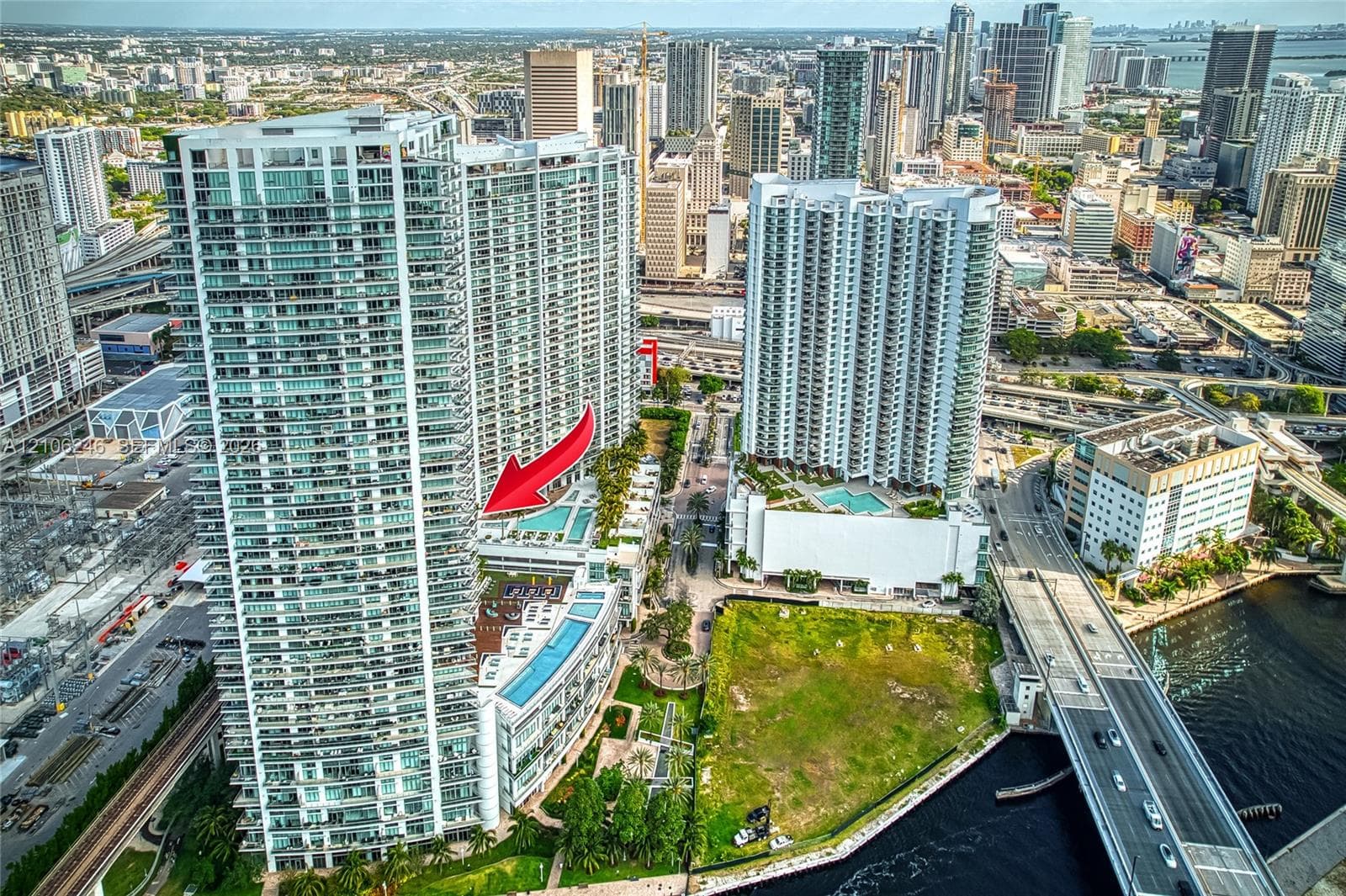 High-rise residential tower featuring a multi-level swimming pool deck, glass balcony railings, floor-to-ceiling windows, and direct urban skyline exposure