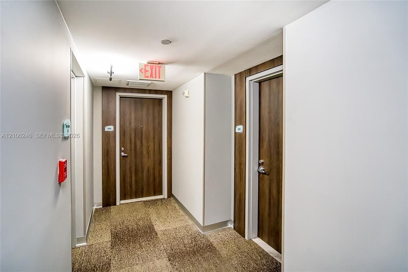 Hallway featuring neutral wall finishes, tile-patterned carpeting, and wood-finish doors set within contrasting dark wood-toned surrounds