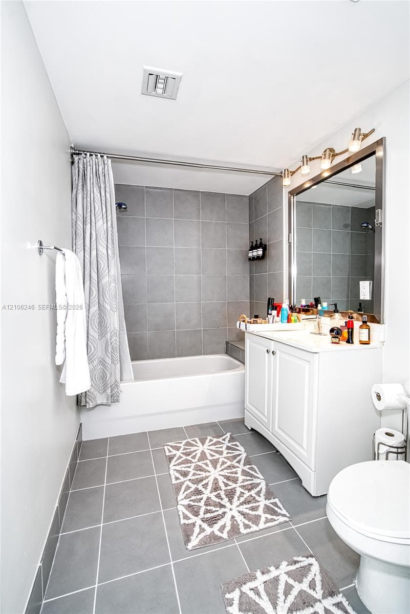 Bathroom featuring a white vanity cabinet, a rectangular mirror with a metal frame, a multi-bulb vanity light fixture, and a bathtub with gray tile surround and flooring