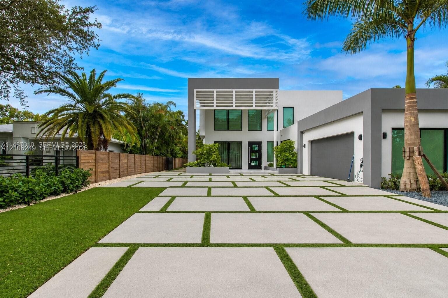 Contemporary two-story exterior featuring a geometric concrete paver driveway with integrated turf, tiered architectural facade, dual-tone masonry, and attached garage