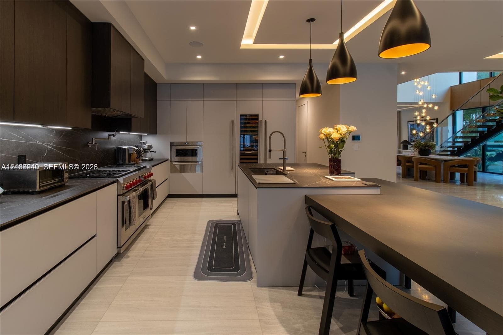 Modern kitchen featuring custom flat-panel cabinetry, dark stone-finish countertops, built-in stainless steel appliances, a large central island with an integrated breakfast bar, and industrial-style pendant lighting