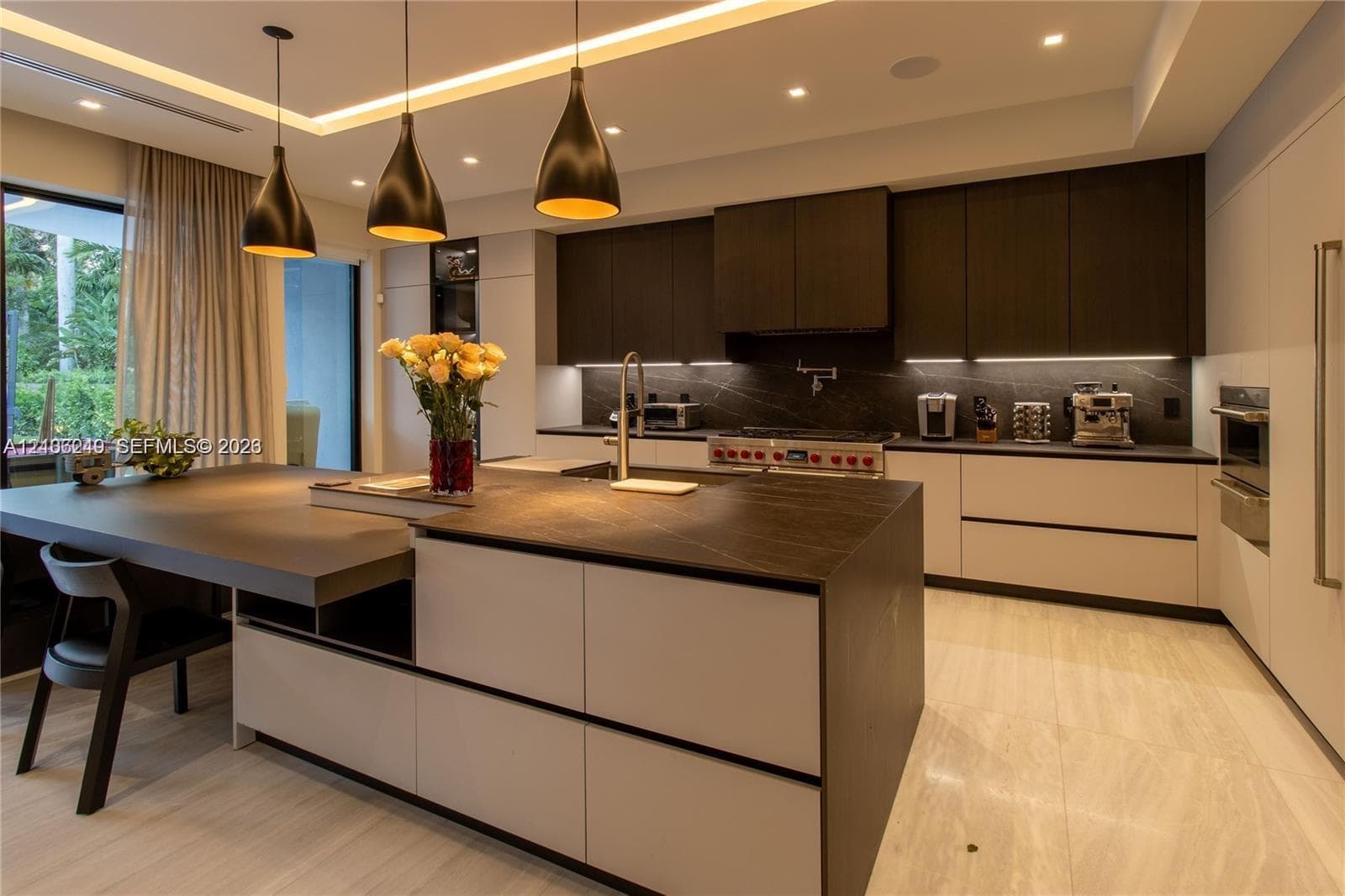 Gourmet kitchen featuring a large central island with stone-finish countertops, matte-finish cabinetry, built-in dual wall ovens, and custom pendant lighting