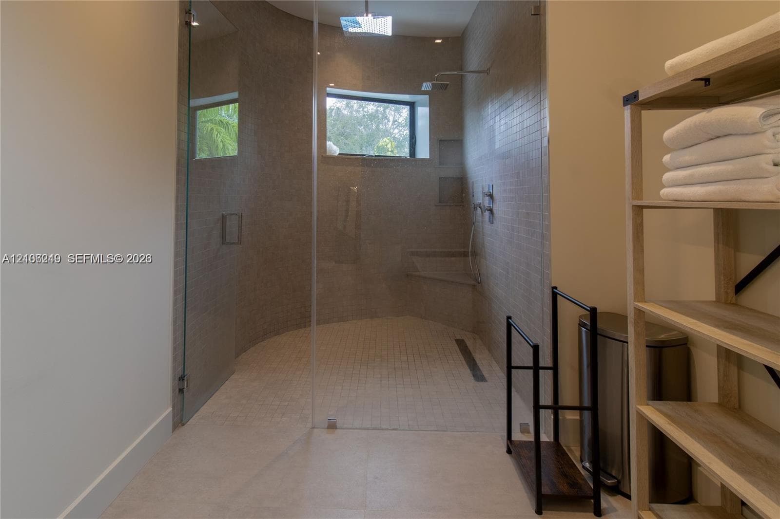 Walk-in shower featuring a glass enclosure, wall-mounted rain shower head, built-in tiled bench, recessed wall shelving, and a linear floor drain