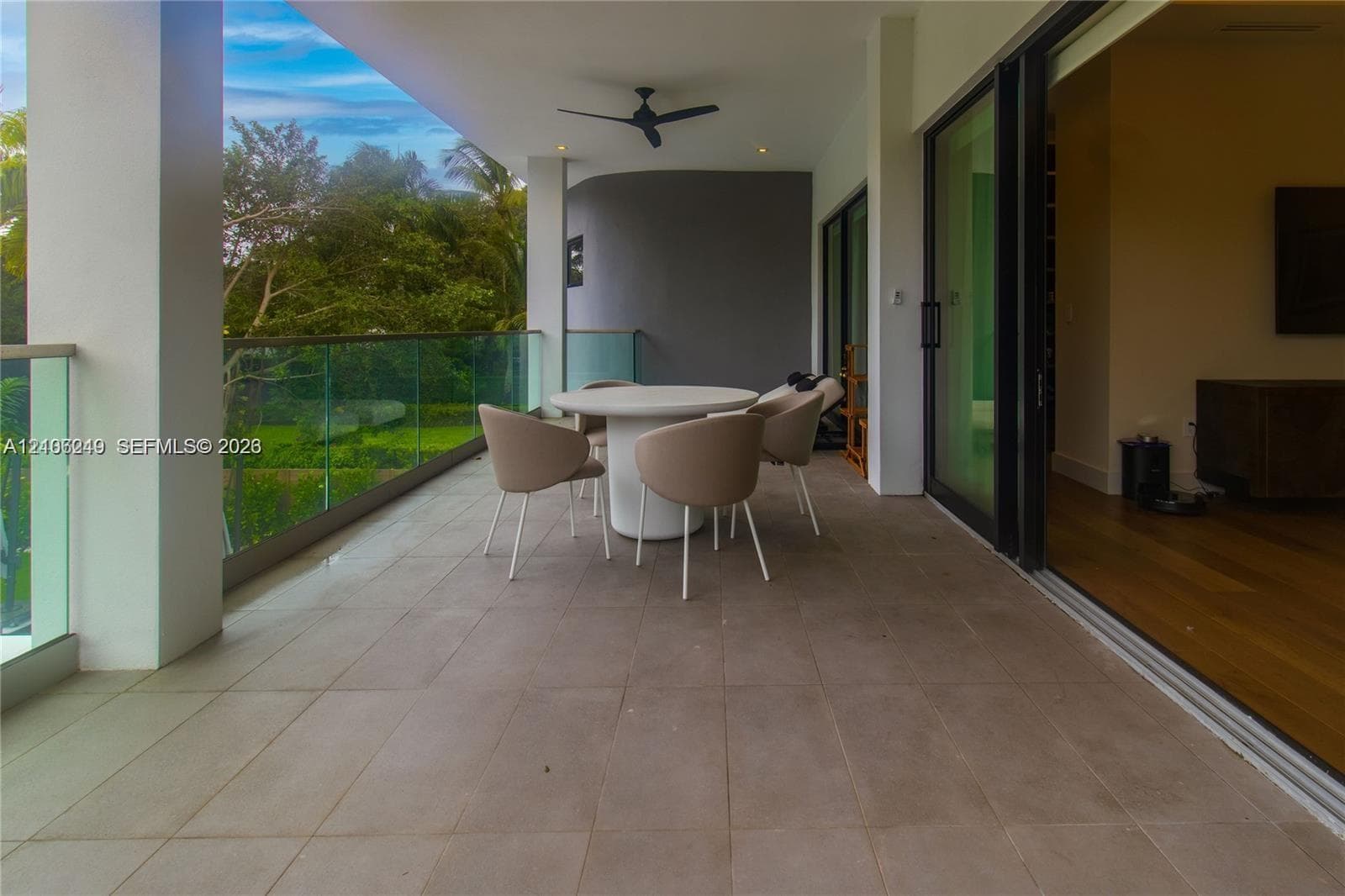 Covered balcony featuring tile flooring, a glass panel railing, a ceiling-mounted fan, and floor-to-ceiling sliding glass doors