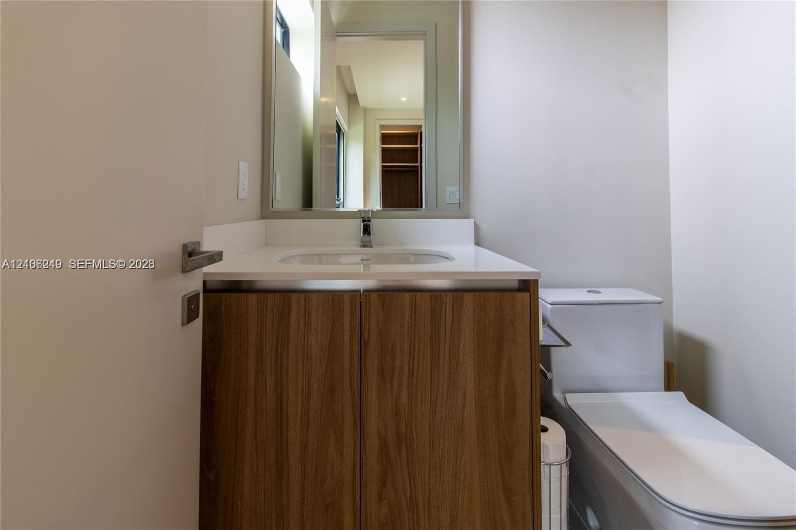 Vanity featuring a wood-finish cabinet, white countertop with an integrated basin, wall-mounted mirror, and chrome faucet