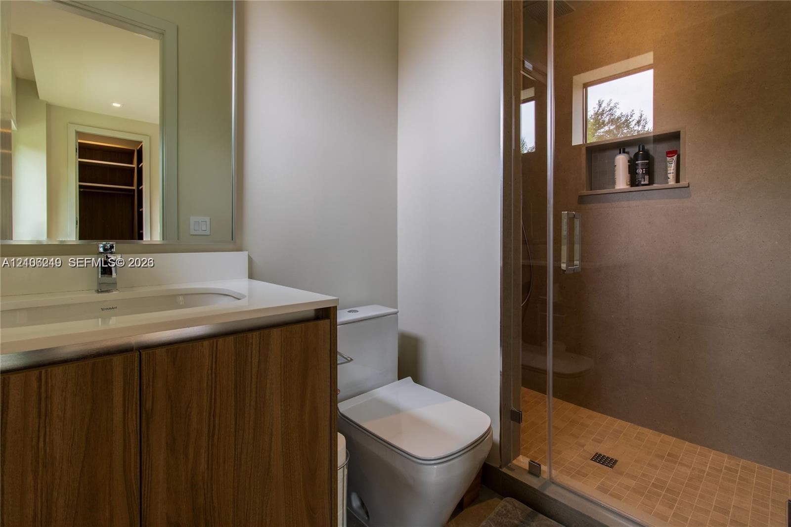 Bathroom featuring a wood-finish vanity with an integrated sink, large frameless mirror, glass-enclosed shower with tiled flooring, and a built-in shower niche