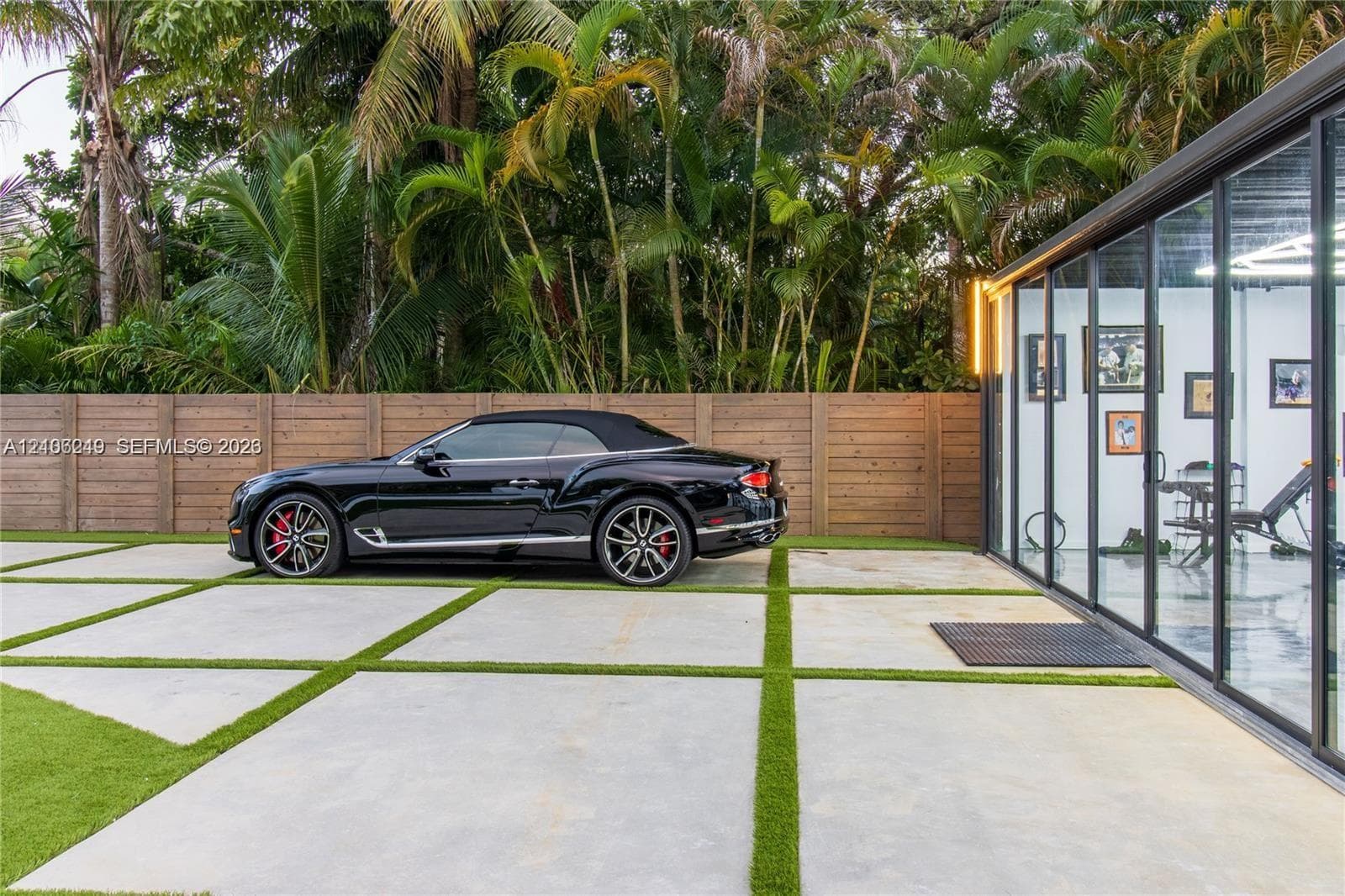 Large-format concrete paver driveway with turf infill, horizontal wood privacy fencing, and floor-to-ceiling glass wall panels