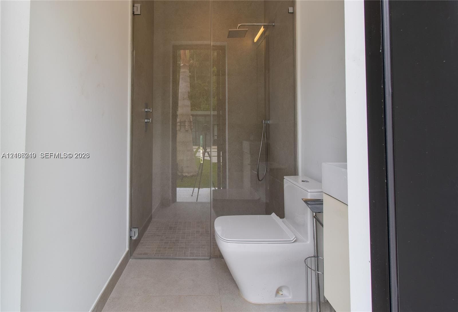 Walk-in shower with frameless glass enclosure, rainfall shower head, handheld sprayer, floor-to-ceiling tile, and wall-mounted dual-flush toilet