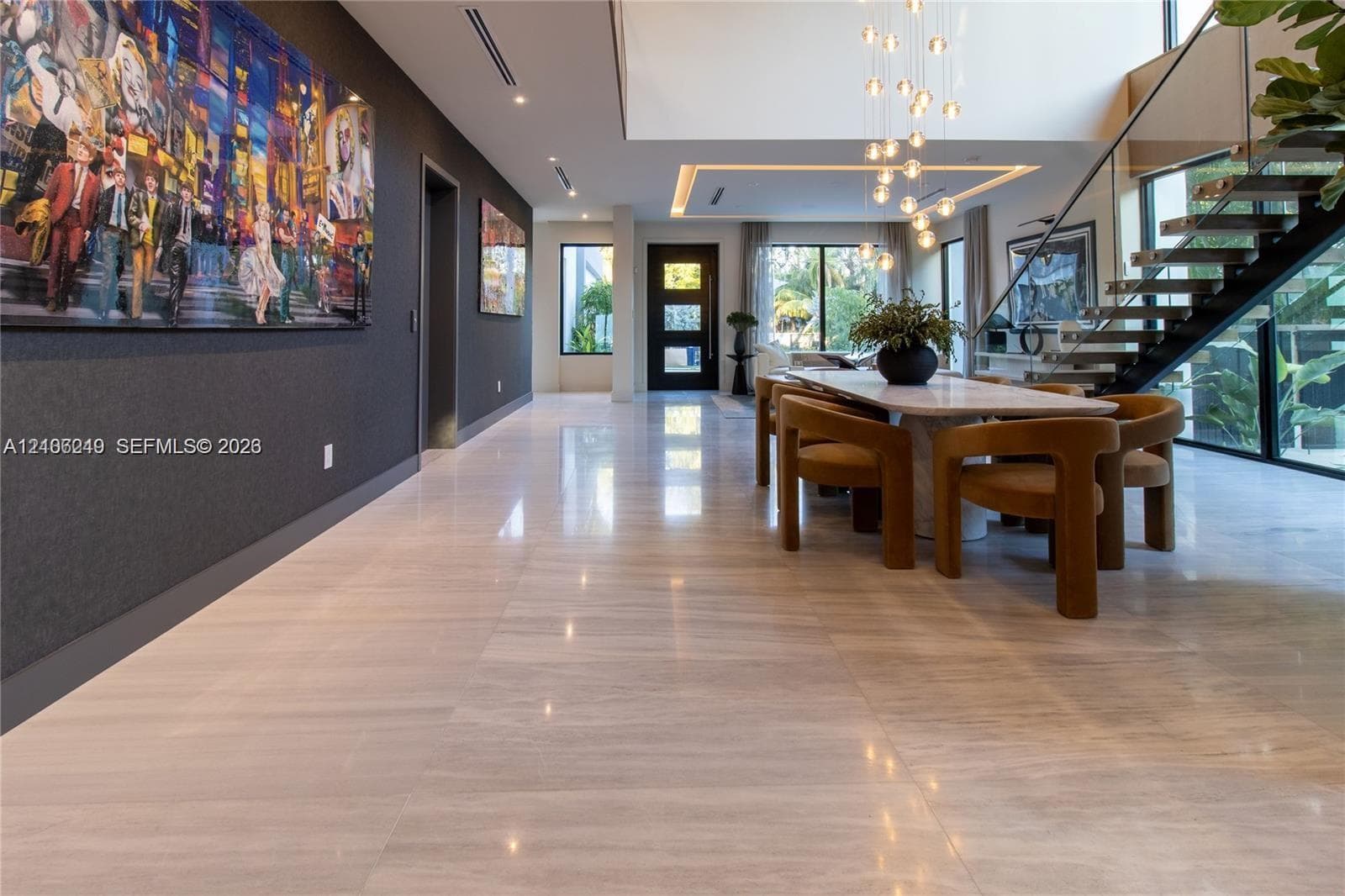 Open-concept interior featuring large-format tile flooring, a double-height ceiling with recessed cove lighting, and a suspended staircase with glass railings and metal treads
