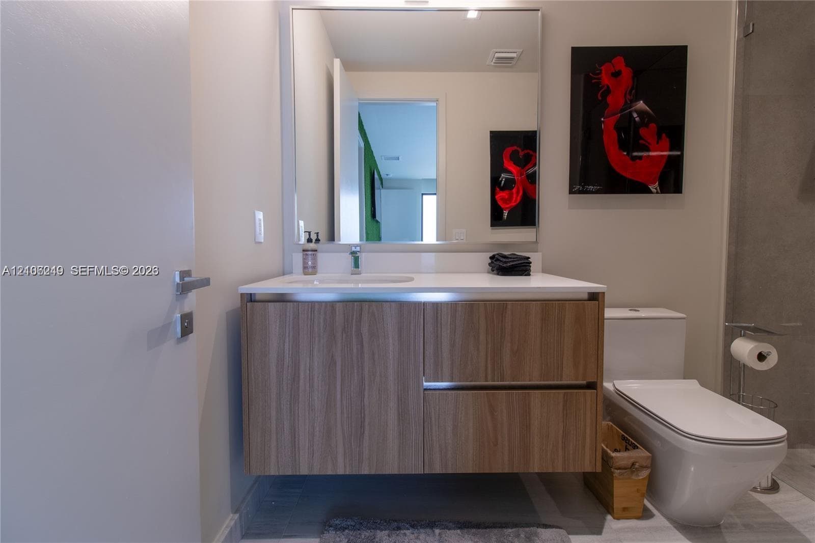 Floating wood-finish vanity with a white countertop, integrated sink, polished chrome faucet, and large rectangular mirror