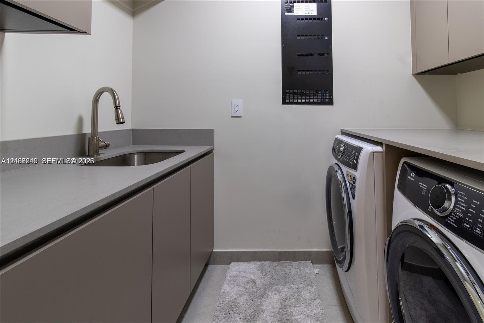 Utility room featuring matte-finish cabinetry, stone-composite countertops, an integrated stainless steel sink with a high-arch faucet, and overhead storage