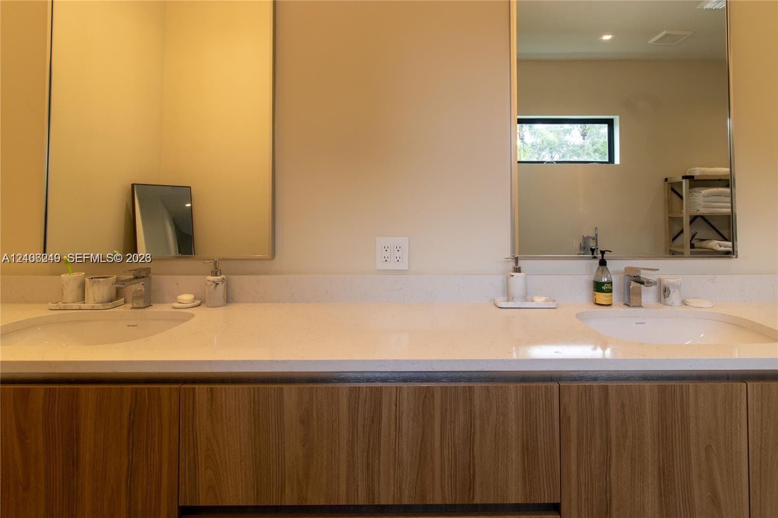 Double vanity featuring a light-toned solid surface countertop, wood-finish cabinetry, two undermount sinks with polished chrome faucets, and dual integrated mirrors