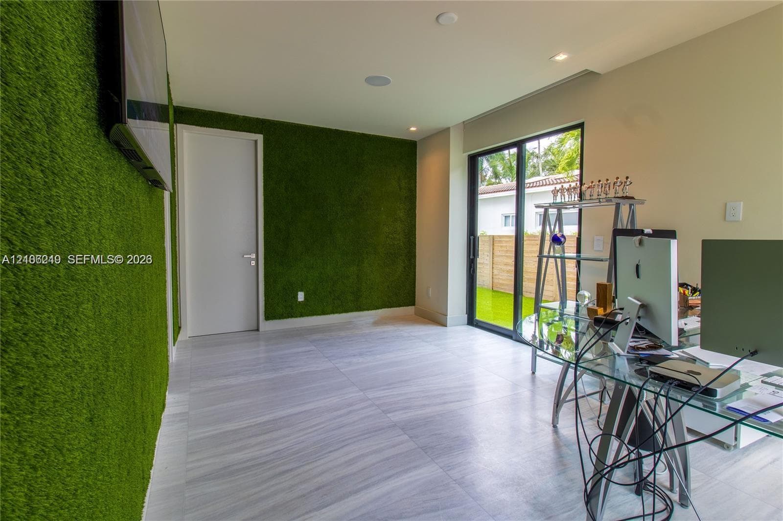 Room featuring textured green wall cladding, neutral large-format tile flooring, recessed ceiling lighting, and sliding glass doors with exterior access