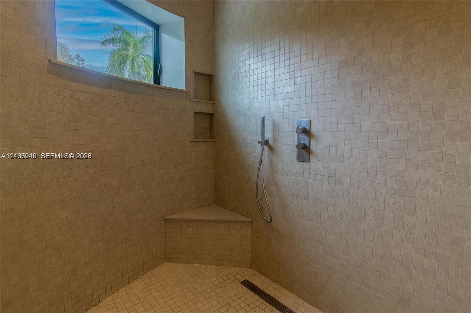 Walk-in shower featuring floor-to-ceiling mosaic tile, built-in corner bench, dual-recessed wall shelving, linear floor drain, and wall-mounted hand-held shower fixture