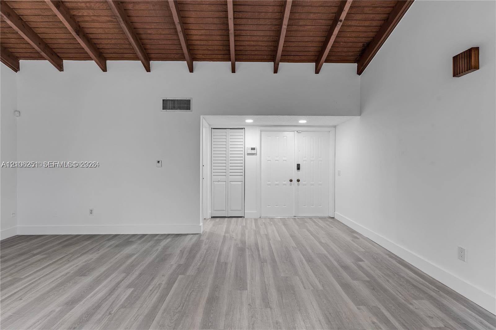 Vaulted ceiling featuring exposed wood beams, neutral walls, wood-finish flooring, and double-entry doors