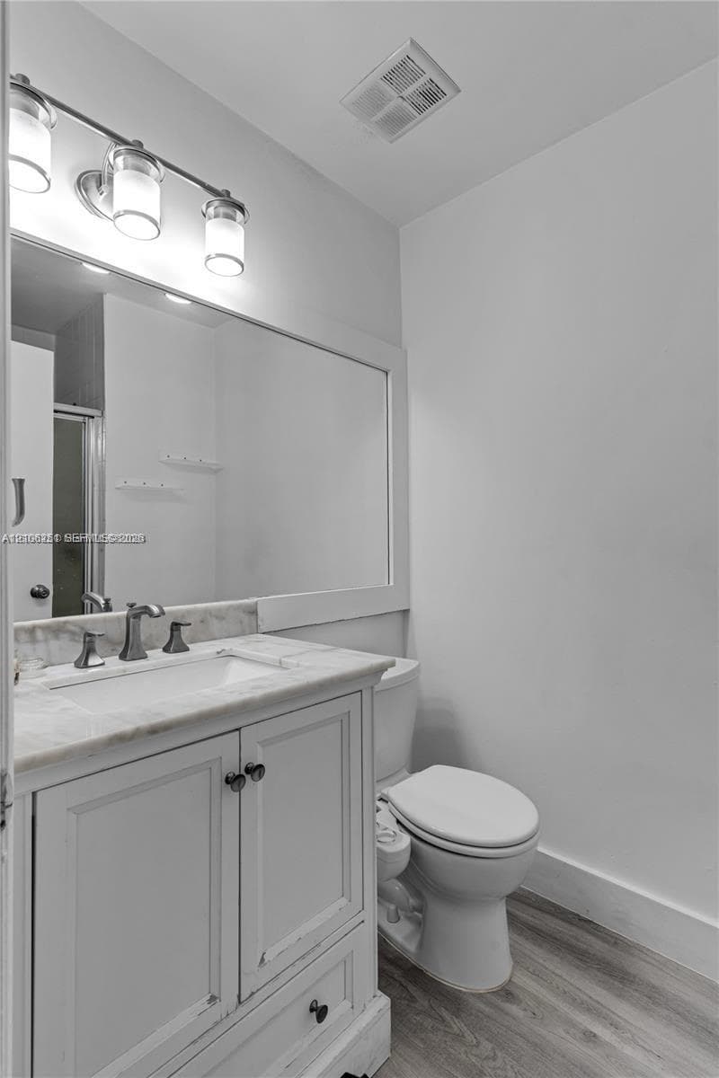 Bathroom featuring a wood-finish vanity with a stone-top integrated sink, a large wall-mounted mirror, a three-light fixture, and wood-finish flooring