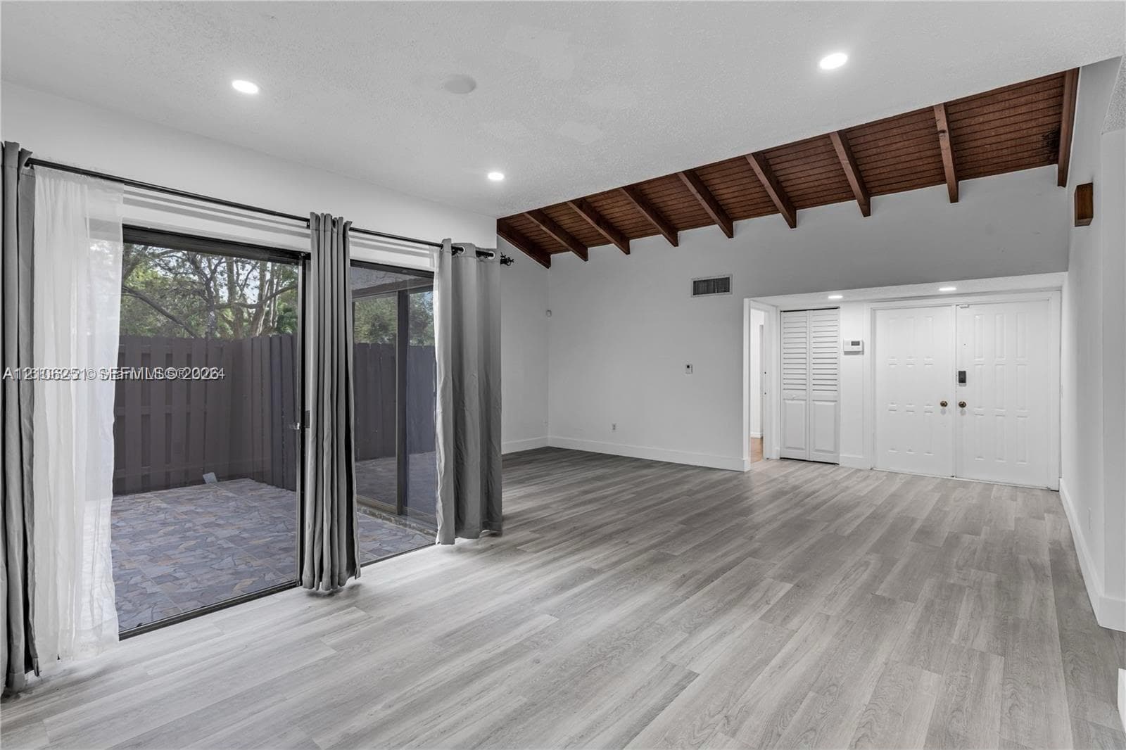 Living area featuring vaulted exposed wood-beam ceilings, wood-finish flooring, recessed lighting, double-door entry, and floor-to-ceiling sliding glass doors