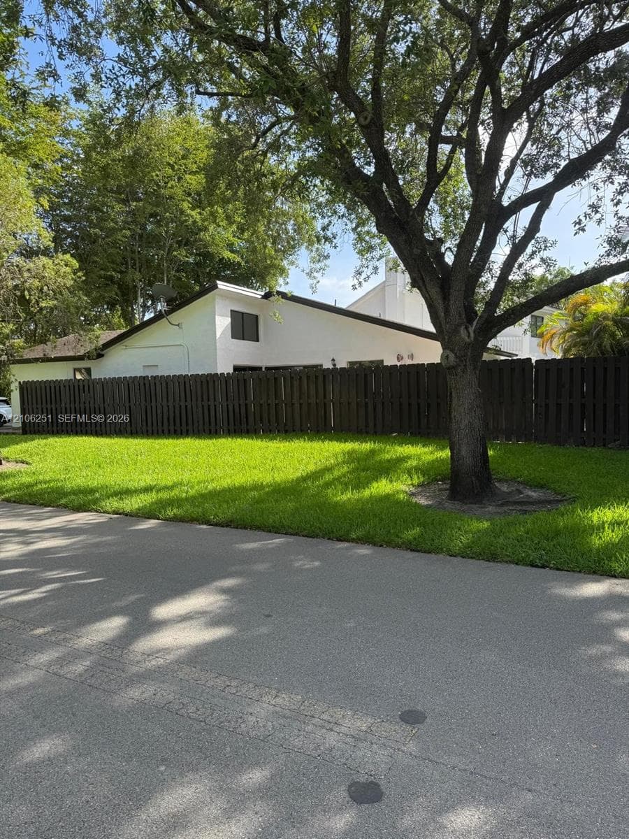 Exterior featuring a white stucco facade, a dark-toned vertical wood privacy fence, and a mature landscape with established trees