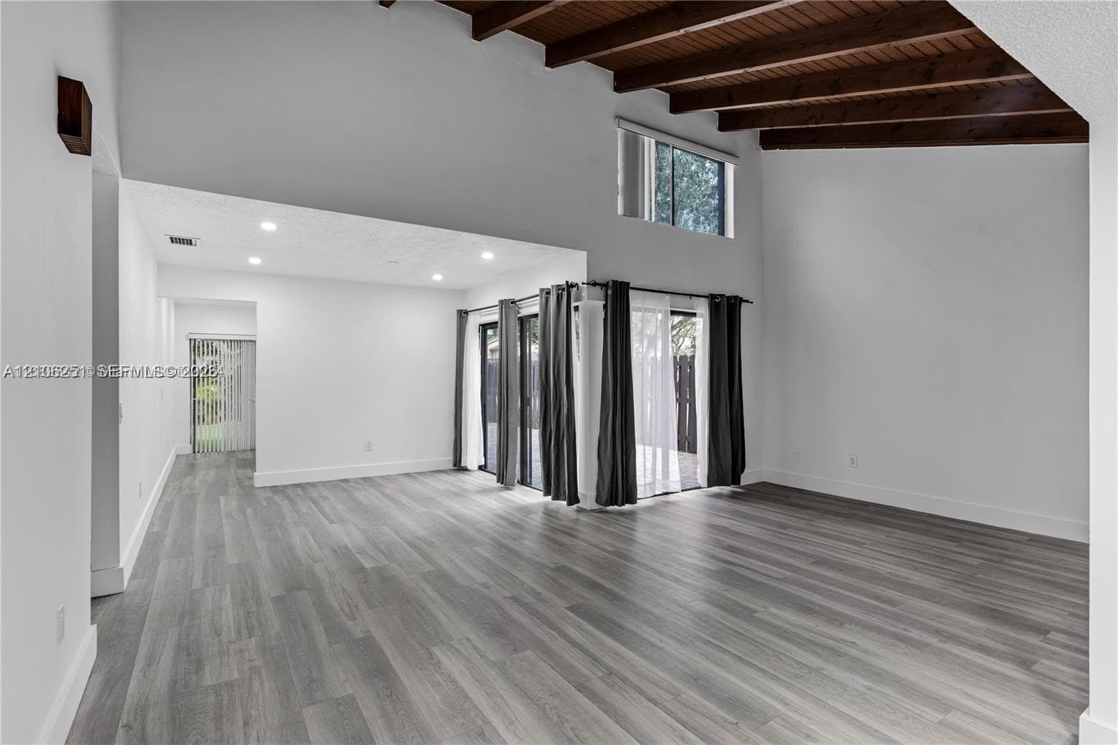 Vaulted ceiling featuring exposed dark wood beams, wood-finish flooring, recessed lighting, and expansive glass sliding doors